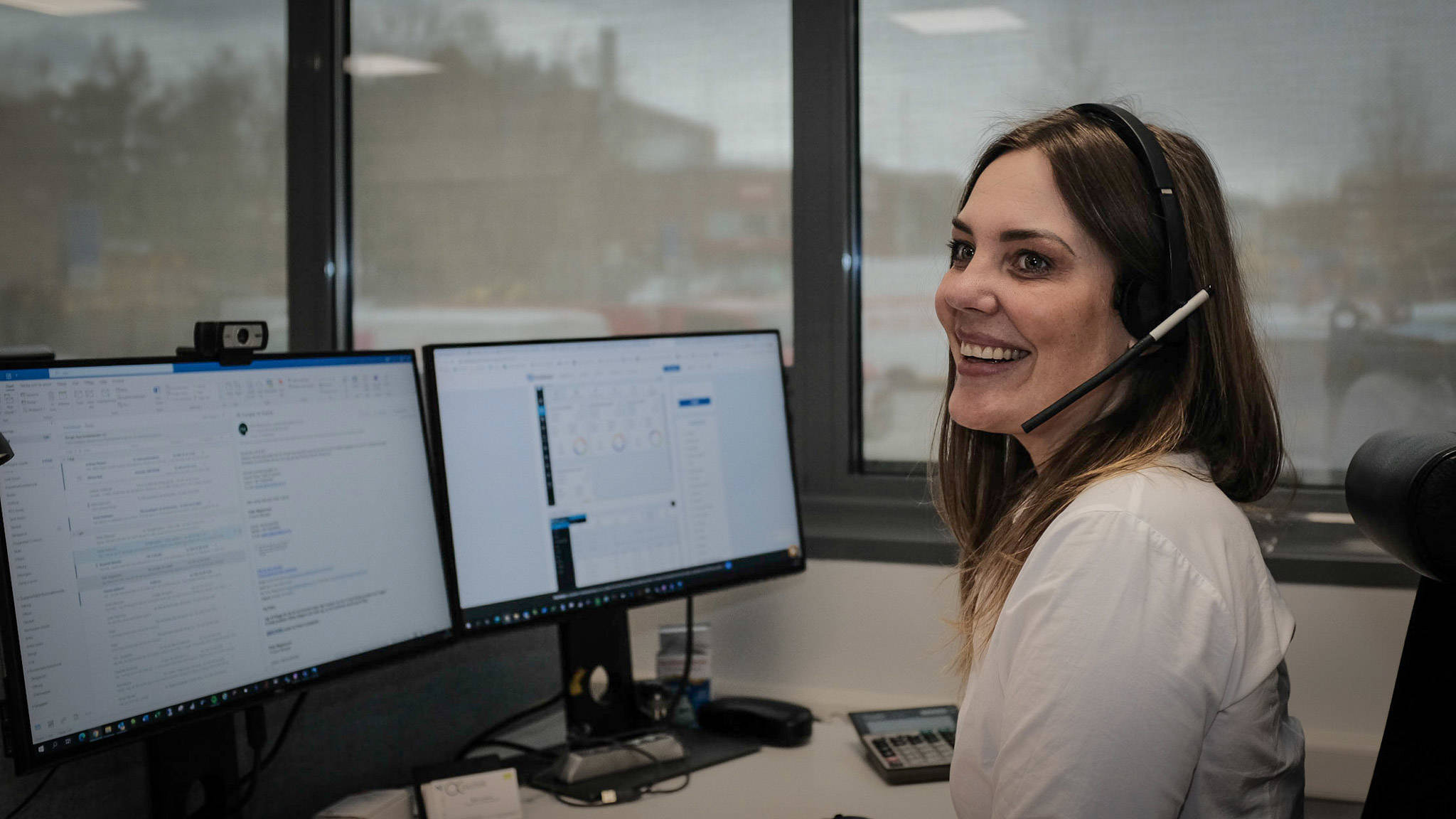 Kvinna med headset sitter vid två skärmar och ger teknisk support, vilket illustrerar effektivt arbete med supportavtal.