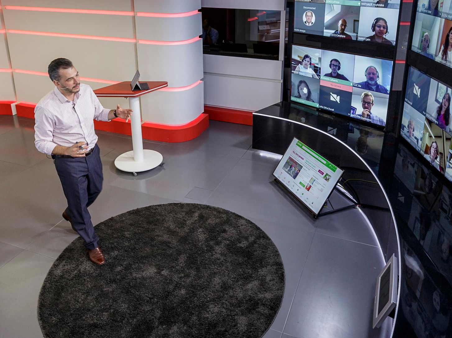 En föreläsare presenterar i ett digitalt klassrum, med flera deltagare på en stor skärm i en modern teknologimiljö.