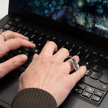 Händer skriver på en laptop med Informationsteknik-logotyp på skärmen