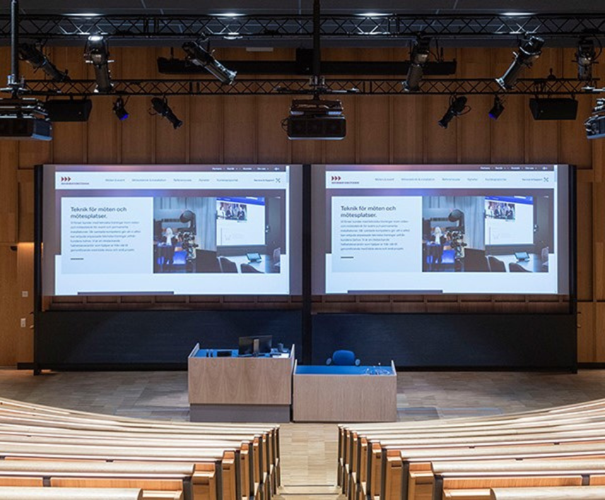 Stort auditorium med dubbla projektordukar och modern teknik för presentationer och möten i en professionell miljö.