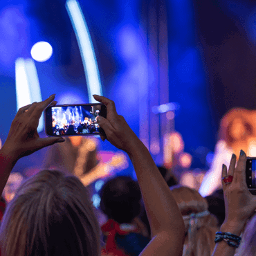 Publikdeltagare på ett event fångar ögonblicket på sina telefoner, med färgglad scenbelysning i bakgrunden.