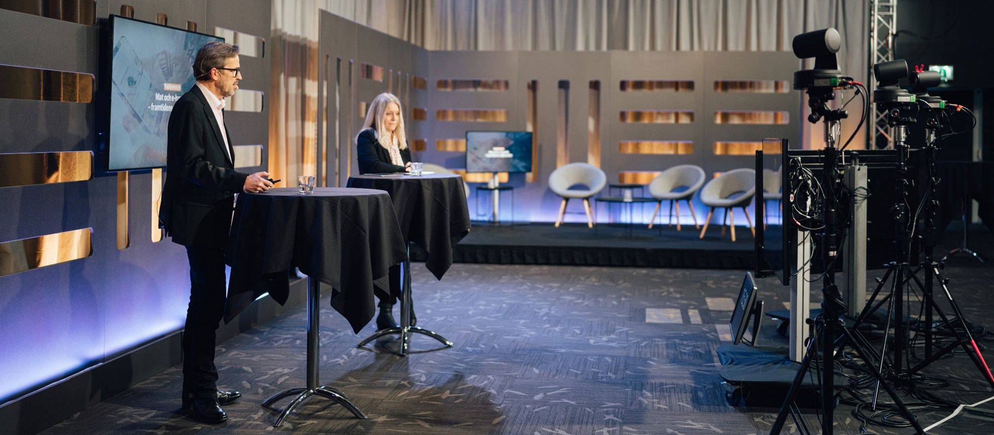 Talare i en studio redo för livesändning, med kameror och scenutrustning i ett modernt och professionellt miljö.